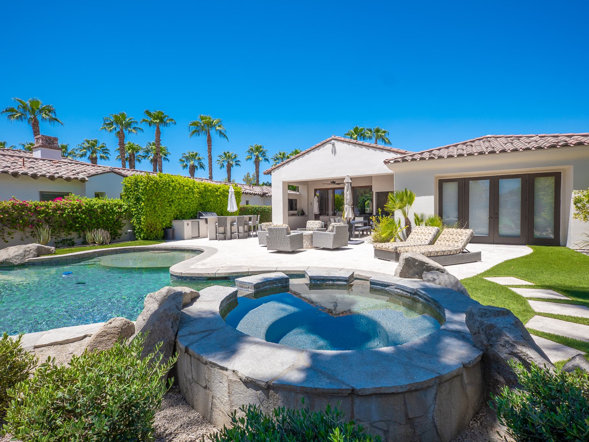 Private pool and rock spa with covered patio lounge under blue desert sky